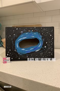 a black hole valentine's box with blue paint on it sitting on top of a counter