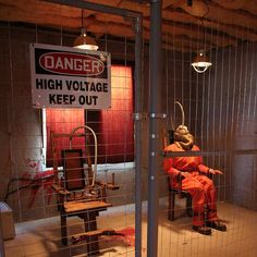 a man in orange jumpsuits sitting on a bench behind a fence with a sign that reads danger high voltage keep out