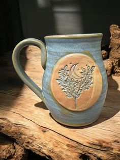 a ceramic mug with a tree and moon design on the side sitting on a piece of wood