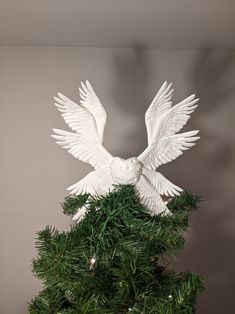 a white bird statue sitting on top of a green christmas tree next to a wall