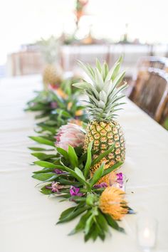 pineapples and other tropical flowers are lined up on a long white tablecloth