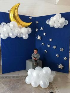 a little boy sitting on a bench in front of a blue backdrop with stars and moon balloons