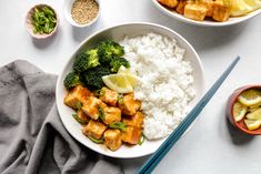 two bowls filled with rice, broccoli and chicken next to chopsticks