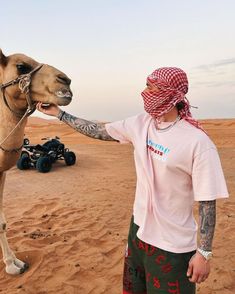 a man with tattoos on his arm petting a camel's nose in the desert