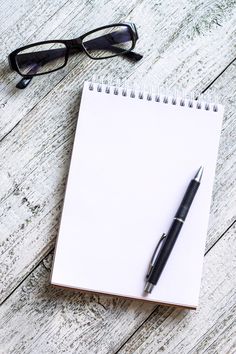 a notepad, pen and glasses on a wooden table