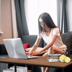 a woman is sitting on the couch with her laptop and books in front of her