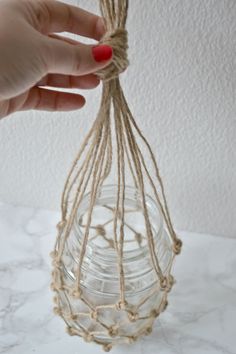 a hand holding a string wrapped glass jar with rope around it on a marble surface