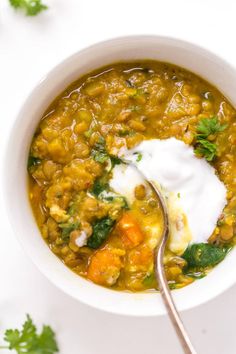 a white bowl filled with lentula soup and topped with sour cream, cilantro and parsley