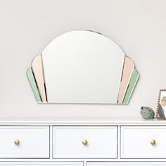 a white dresser topped with a mirror next to a wall mounted shelf filled with drawers