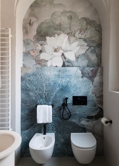 a toilet and sink in a bathroom with flowers painted on the wall above it's tank