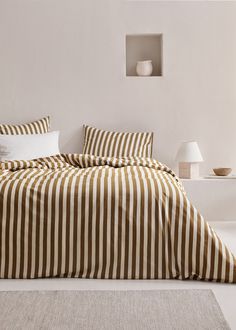 a bed with striped sheets and pillows in a white room next to a lamp on the floor