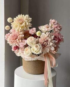 a basket filled with lots of flowers on top of a white cake covered in pink ribbon