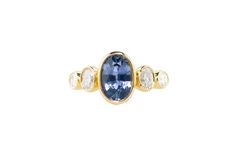 an oval blue sapphire and diamond ring with three diamonds on the sides, set in yellow gold