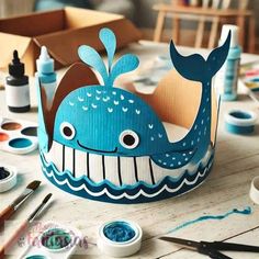 a blue whale crown sitting on top of a wooden table next to paint and brushes