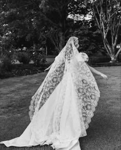 a woman in a wedding dress is walking through the grass with her veil over her head