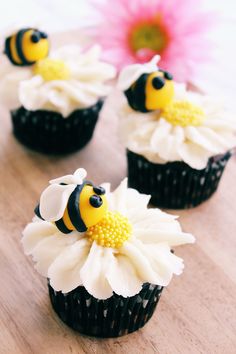 three cupcakes with white frosting and yellow decorations on top are sitting on a table