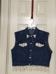 a denim vest hanging on a door with white trimmings and beaded details