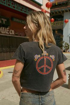 Mineral washed graphic t-shirt. Vintage-style back graphic print with peace sign and flowers. Chest print with flower and "Made With Love" text. Round neckline. Short sleeves. Lettuce-edge cuffs and hem. Cropped length. Relaxed fit. 100% Cotton. Imported top designed and printed in LA. Model wears size S. Peace Sign Tee Shirt, Floral Peace Sign, Graphic Baby Tee, Baby Graphic Tees, Love Text, Peace Sign, Baby Tee, Made With Love, Infant Tees