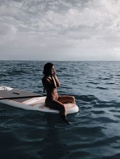 a woman sitting on top of a surfboard in the ocean while talking on a cell phone