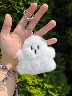 a hand holding a white fluffy keychain with a ghost face on it's side