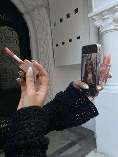 a woman taking a selfie with her cell phone while holding some lipstick in one hand