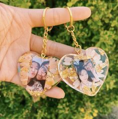 two heart shaped key chains with pictures on them in front of some bushes and trees