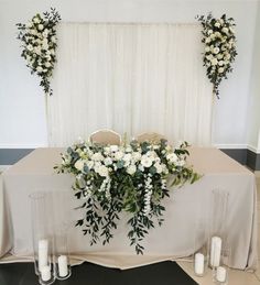 a table with white flowers and candles on it in front of a curtained wall