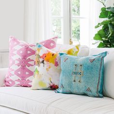 three colorful pillows sitting on top of a white couch next to a potted plant