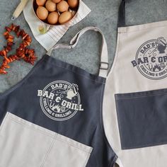 two aprons with logos on them next to some eggs