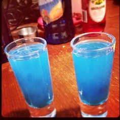 two glasses filled with blue liquid sitting on top of a wooden table