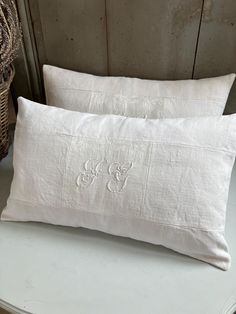 two white linen pillows with mickey mouse embroidered on the front and back, sitting next to a wicker basket