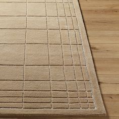 a beige area rug with squares and lines on the top, in front of a wooden floor