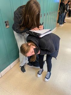 two girls are writing on paper in a hallway next to lockers with blue doors