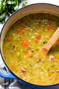 a blue pot filled with soup next to a wooden spoon and some parsley on the side