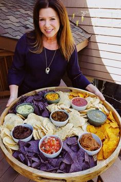 a woman sitting in front of a wooden tray filled with chips and salsa