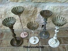 four candlesticks sitting on top of a tile floor next to a stone wall