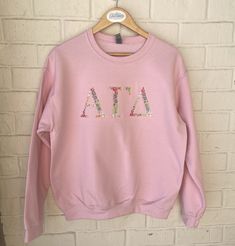 "Alpha Gamma Delta Greek Letter Sweatshirt The letters are 4-4.5\" depending on the size of the sweatshirt.   Letters are completely embroidered in floral font in pastels.  All embroidery is stabilized and has a soft cover fabric backing the embroidery to be soft against the skin.  Sweatshirt letters will look exactly as shown in the same colors.  ~~Sweatshirts used are Gildan Heavy Blend in Pink 8 oz./yd² (US) 13.3 oz./L yd (CA), 50/50 cotton/polyester, 20 singles Classic fit Air jet yarn for s Sorority Sweatshirt With Letter Print In Relaxed Fit, Sorority Long-sleeve Cotton Sweatshirt, Cotton Sorority Sweatshirt With Long Sleeves, Spring Sorority Long Sleeve Tops, Cotton Long Sleeve Sorority Sweatshirt, Sorority Letter Print Sweatshirt In Relaxed Fit, Spring Sorority Long Sleeve Sweatshirt, Sorority Long Sleeve Tops For College, Sorority Long Sleeve Relaxed Fit Tops