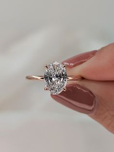 a woman's hand holding an engagement ring with a diamond in the center, on a white background