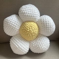 a crocheted white flower sitting on top of a gray couch next to a pillow