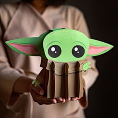 the child yoda paper toy is held in front of a woman's face