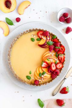 a cheesecake topped with sliced peaches and strawberries on a white plate next to other fruit