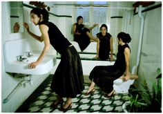 a woman in a black dress sitting on a toilet next to a sink and three other women