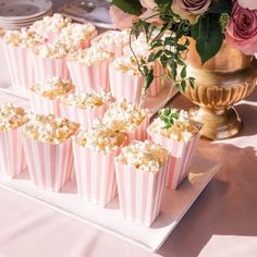 pink and white striped cupcakes are on a tray next to a gold vase with flowers