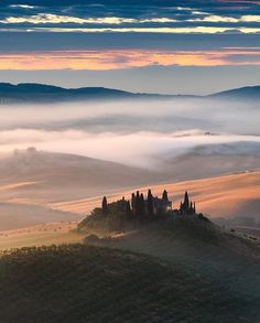 the rolling hills are covered in fog and low lying clouds as the sun is setting