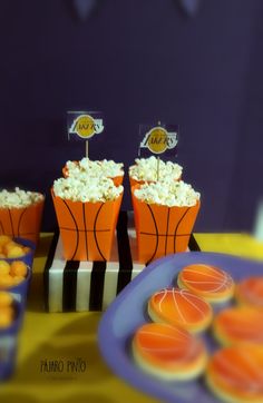 an orange and black table topped with cupcakes next to plates filled with popcorn