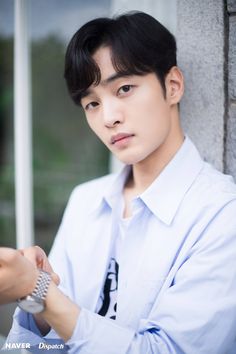 a young man in a white shirt is leaning against a wall and looking at his watch