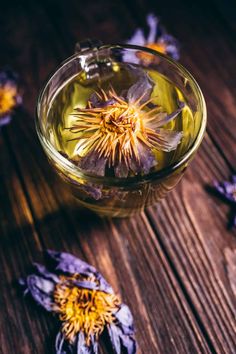 a glass bowl filled with water and purple flowers on top of a wooden table next to it