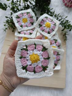 a hand holding four crocheted coasters with flowers on them