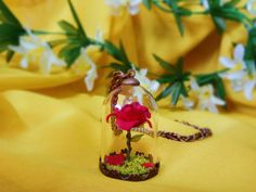 a small glass bell jar with a red rose in it on a yellow fabric background