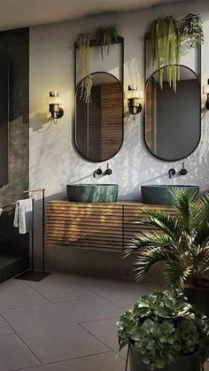 a bathroom with two sinks and three mirrors on the wall next to potted plants